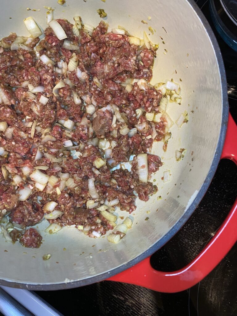 red dutch oven filled with beef, onions, garlic, and spices