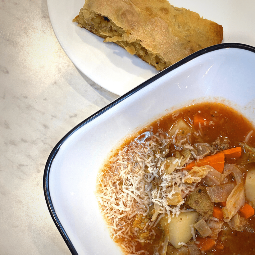 bowl of cabbage and beef soup next to a plate of bread