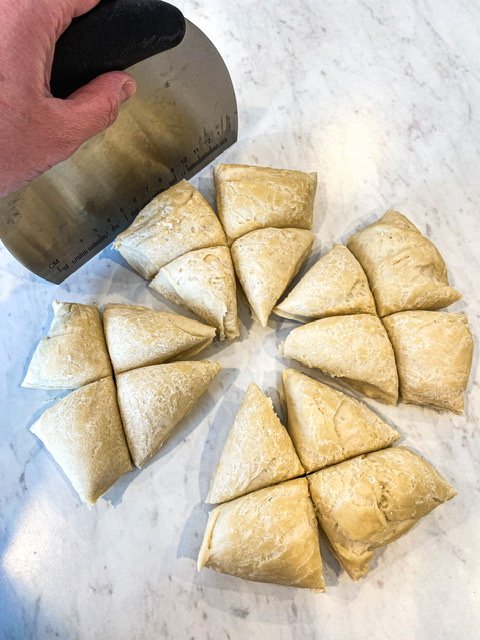 A dough scraper is shown cutting a large sourdough discard tortilla dough ball into 16 equal portions on a white counter.