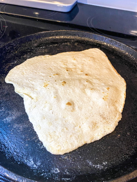 A sourdough discard tortilla is being cooked on a cast iron griddle.