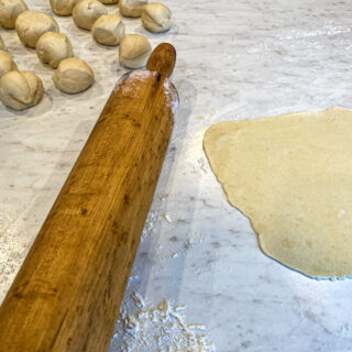 a wooden rolling pin is sitting on a white countertop between balls of sourdough and a rolled out discard sourdough tortilla