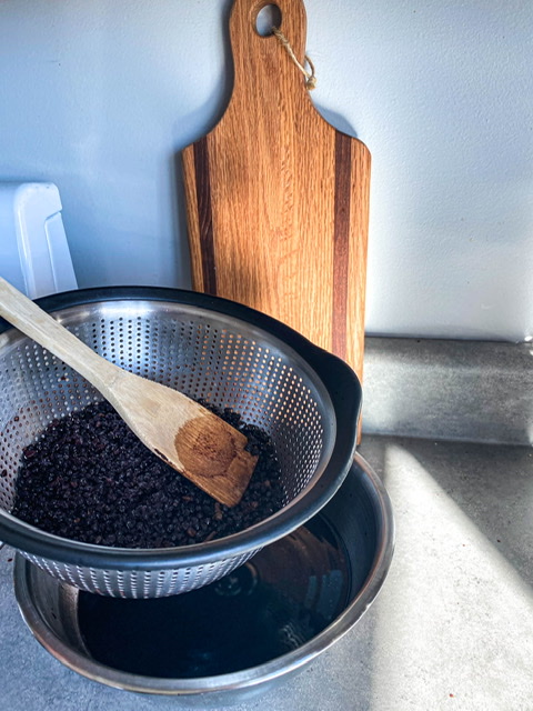 elderberries being strained from the liquid in stainless strainer and bowl