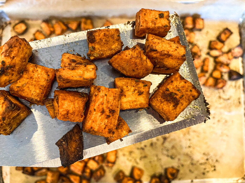 Stainless spatula holding a small serving over a tray of savory sweet potatoes.