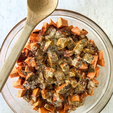 glass bowl on a white counter with a wooden spoon on the edge and filled with diced savory sweet potatoes