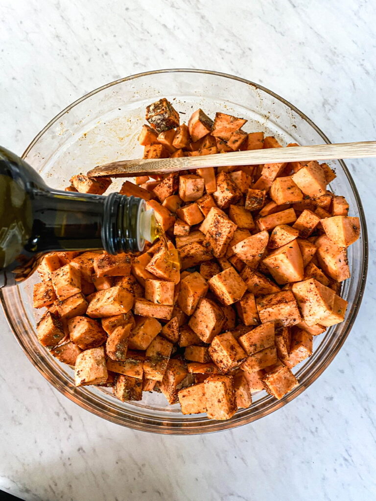 bowl of savory sweet potatoes being drizzled with olive oil