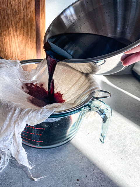 purple liquid being poured through a cheesecloth into a glass measuring cup