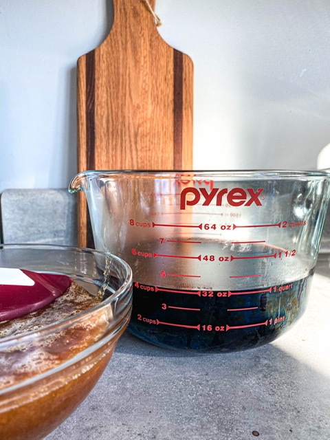 4 cups of elderberry juice sitting next to a glass bowl full of honey