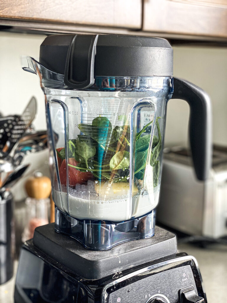 vitamix filled with spinach, milk, and apples