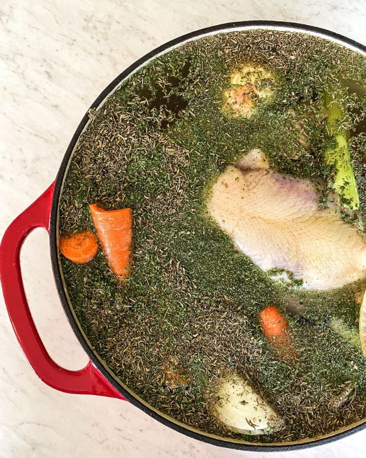 nourishing bone broth on the stove with a whole chicken