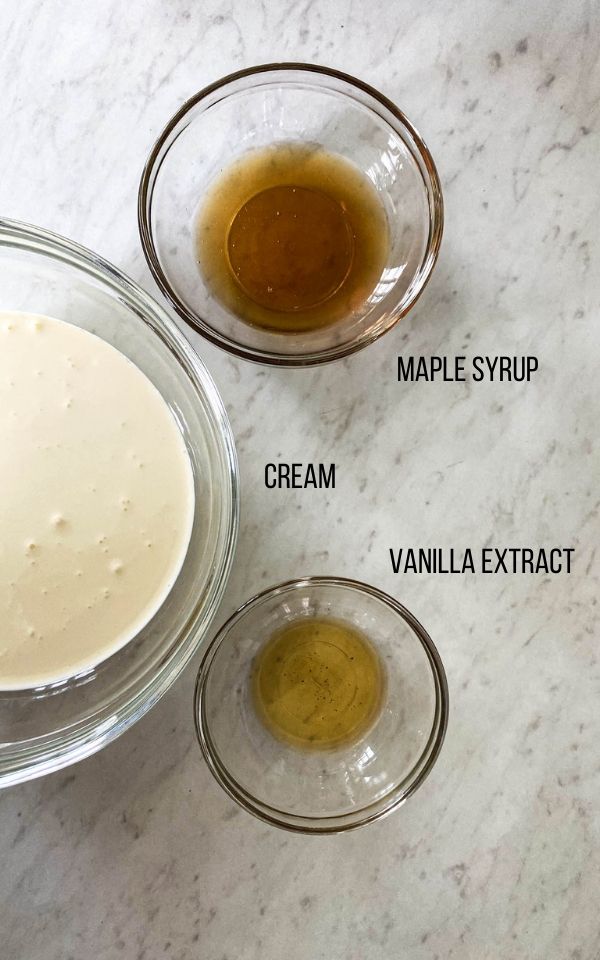 three glass bowls on a white counter filled with cream, maple syrup, and vanilla extract
