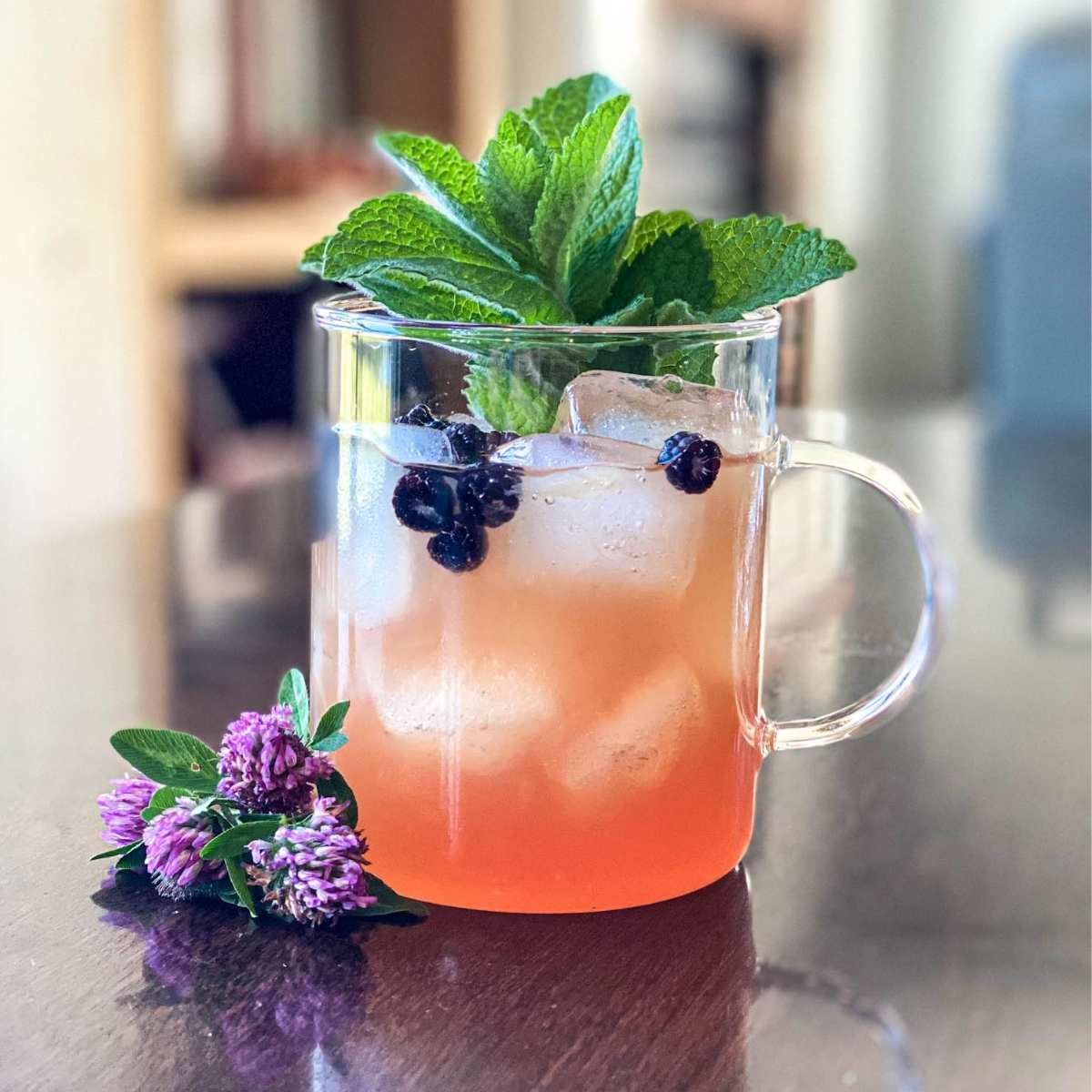 clear mug filled with foraged red clover lemonade garnished with red clover, mint, and wild black raspberries