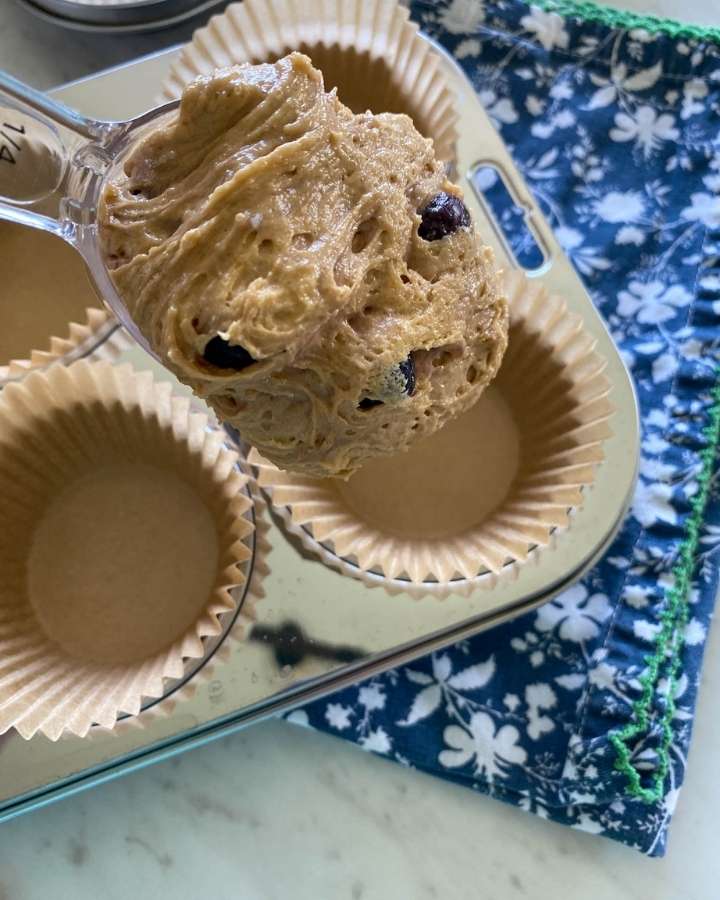 sourdough blueberry muffin batter being spooned into muffin tins