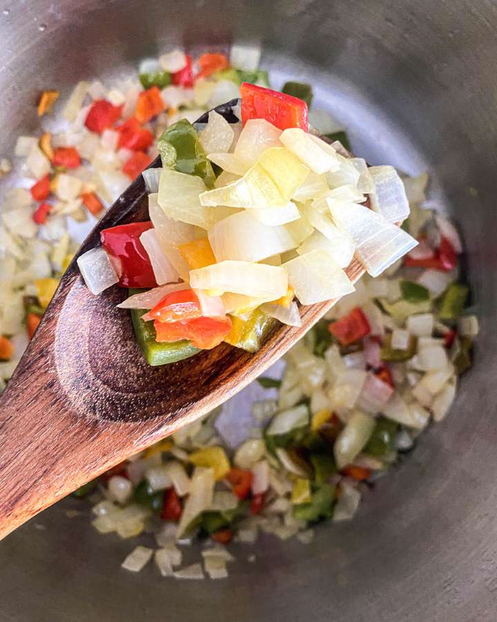 wooden spoon holding sautéed onions and peppers