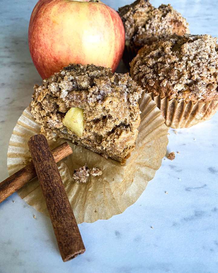 sourdough apple spice muffins on a white counter next to an apple and cinnamon sticks