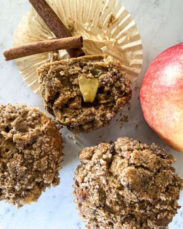 sourdough apple spice muffins sitting on a white counter next to an apple