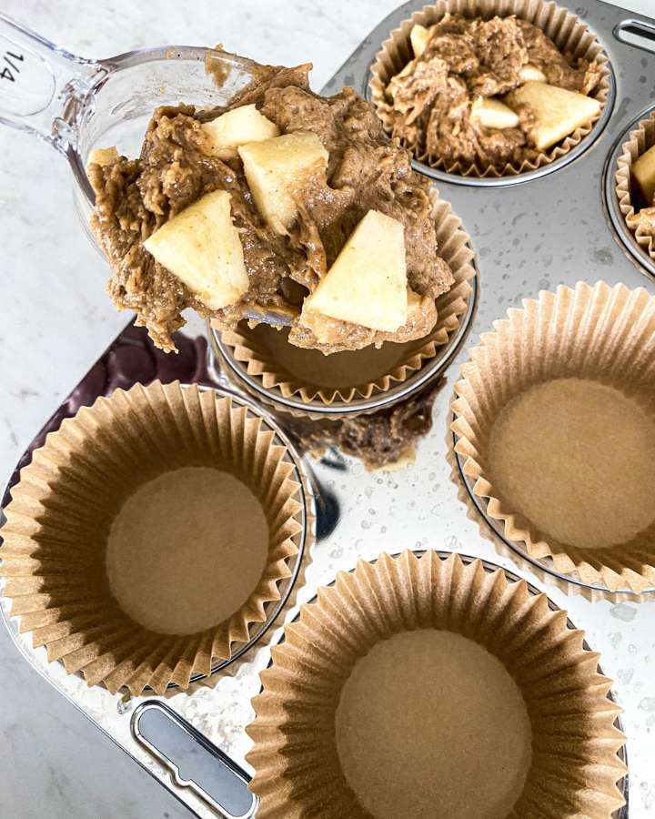 muffin tin being filled with sourdough apple spice muffin batter