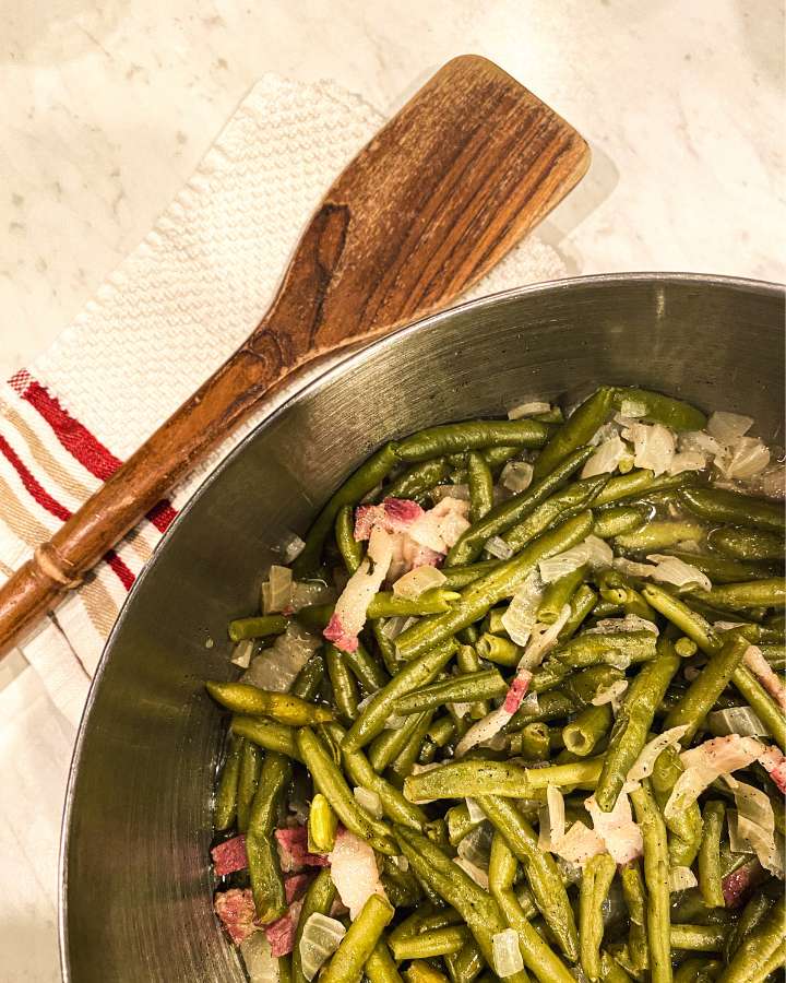 cooked green beans in a stock pot next to a wooden spoon