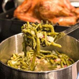 green beans on a serving spoon held in front of a turkey