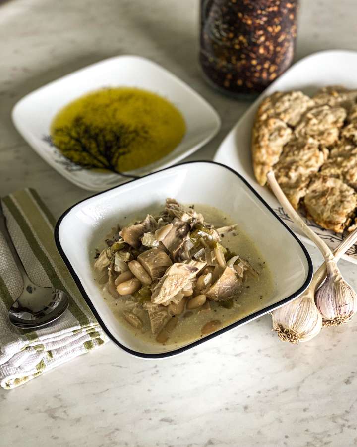 bowl of chicken chili on a white counter with bread and oil