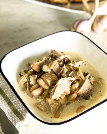 bowl of chicken chili on a white counter next to garlic and bread