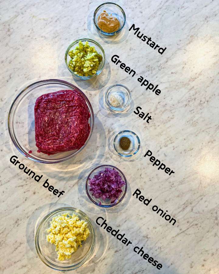 apple cheddar beef burger ingredients on glass bowls on a white counter