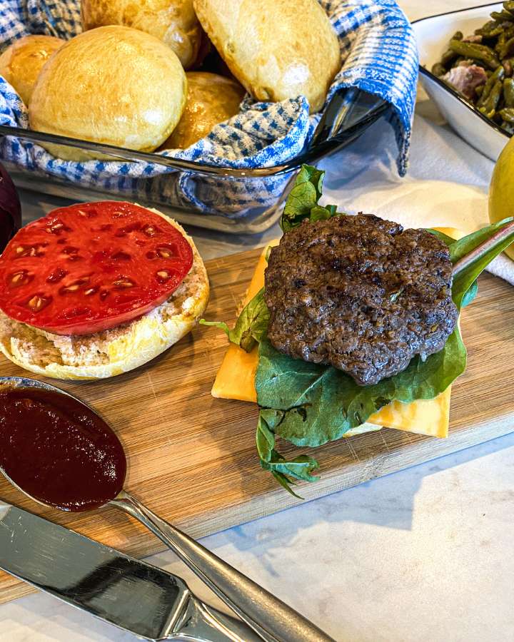 apple cheddar beef burger on a wooden cutting board with toppings and a bun