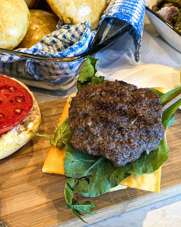 apple cheddar beef burger on a wooden cutting board with toppings and a bun