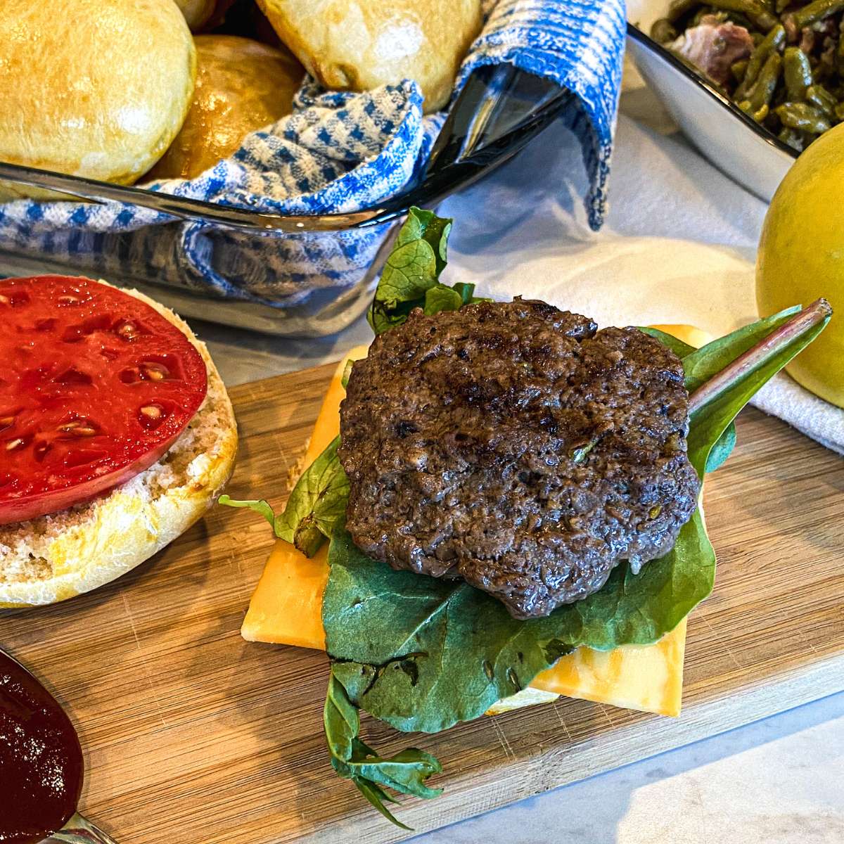 apple cheddar beef burger on a wooden cutting board with toppings and a bun