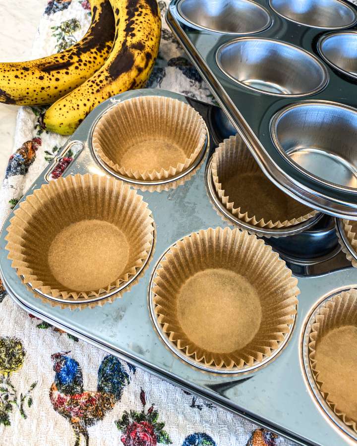 muffin tins with parchment paper liners on a towel with chickens next to a pile of bananas