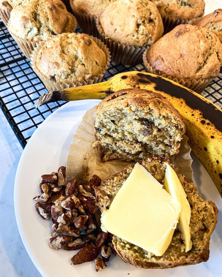 banana muffins on a cooling rack next to a banana and chopped pecans