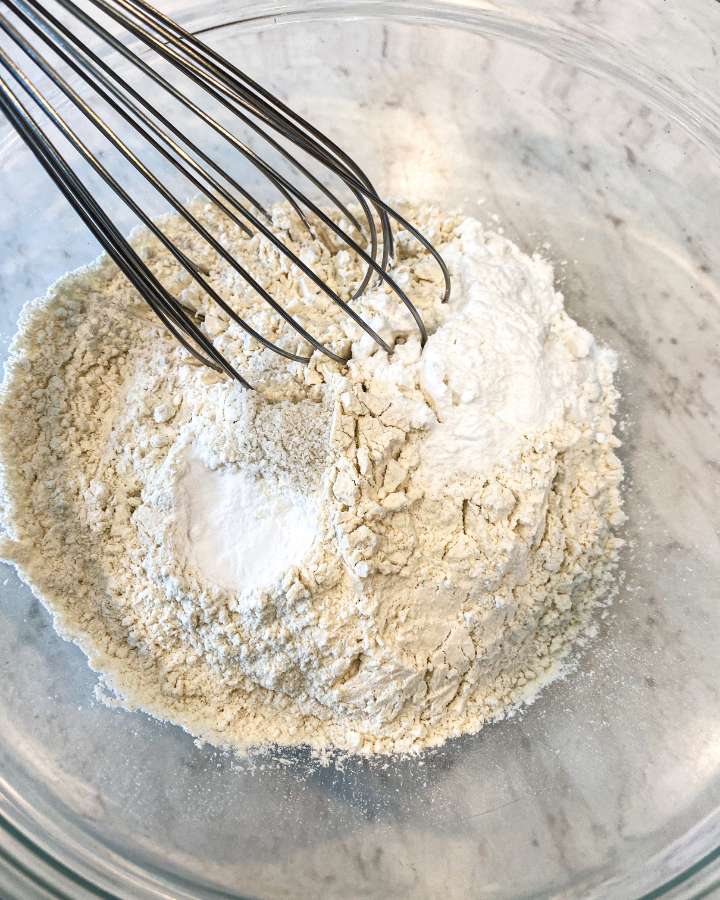 glass bowl filled with flour and a whisk stiring it