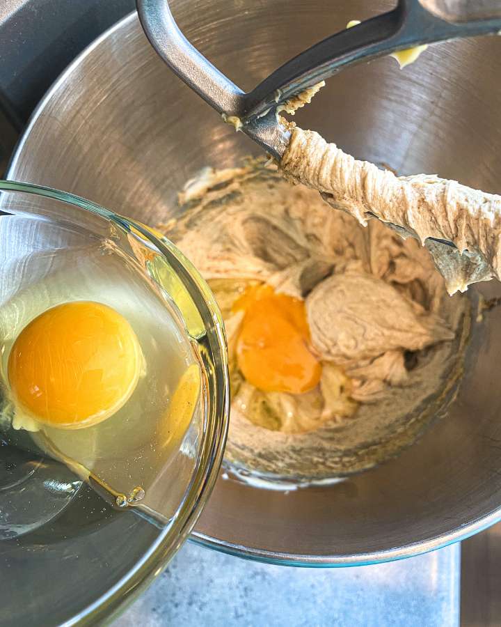 eggs being poured into banana muffin batter in a mixing bowl