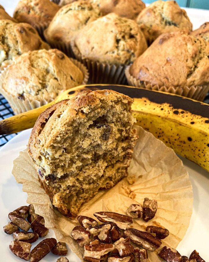 banna muffins on a cooling rack next to a banana and chopped pecans