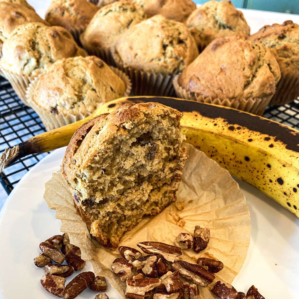 banna muffins on a cooling rack next to a banana and chopped pecans