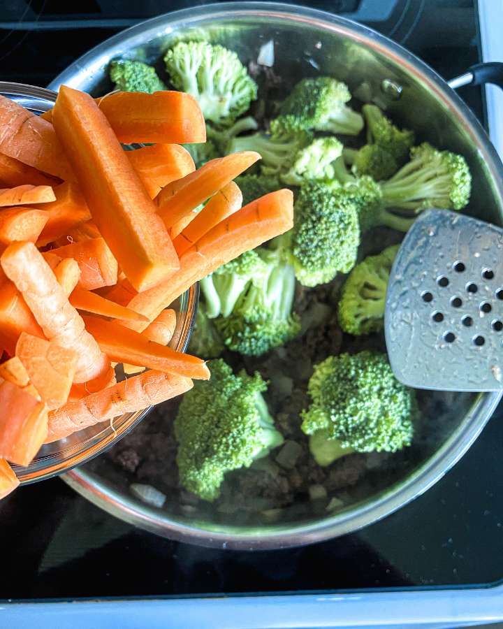 carrots being poured into a skillet of broccoli and beef