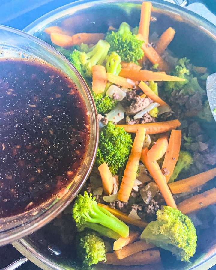 beef, broccoli, and carrots in a skillet with sauce being poured into the skillet