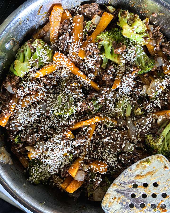 beef and broccoli stir fry topped with sesame seeds in a stainless skillet